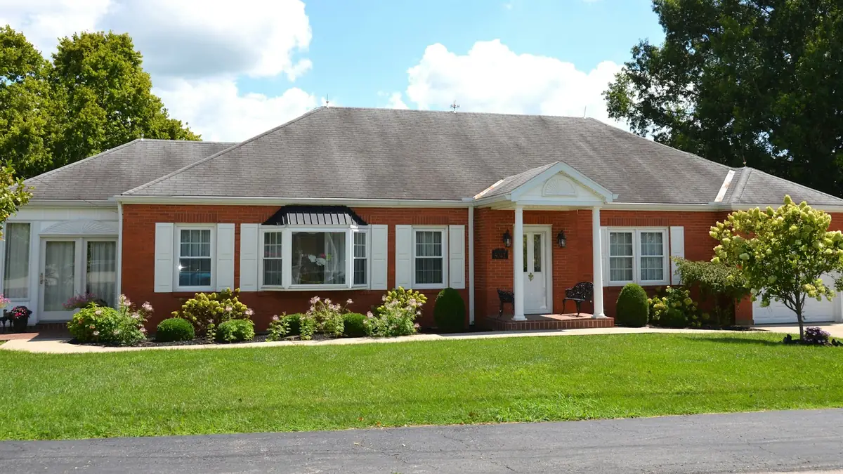 A single-story red brick ranch house with white shutters and a clipped lawn - Leak Detection in Petersburg