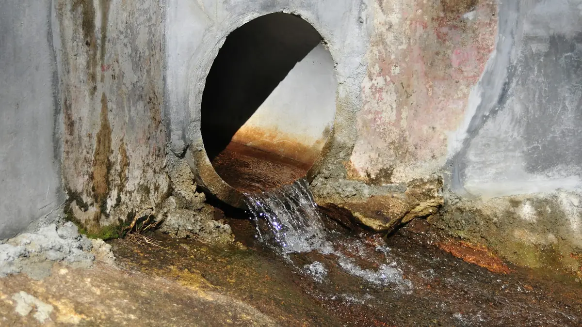 Water running out of a round concrete pipe opening, rust stains on the wall - Leak Detection in Petersburg